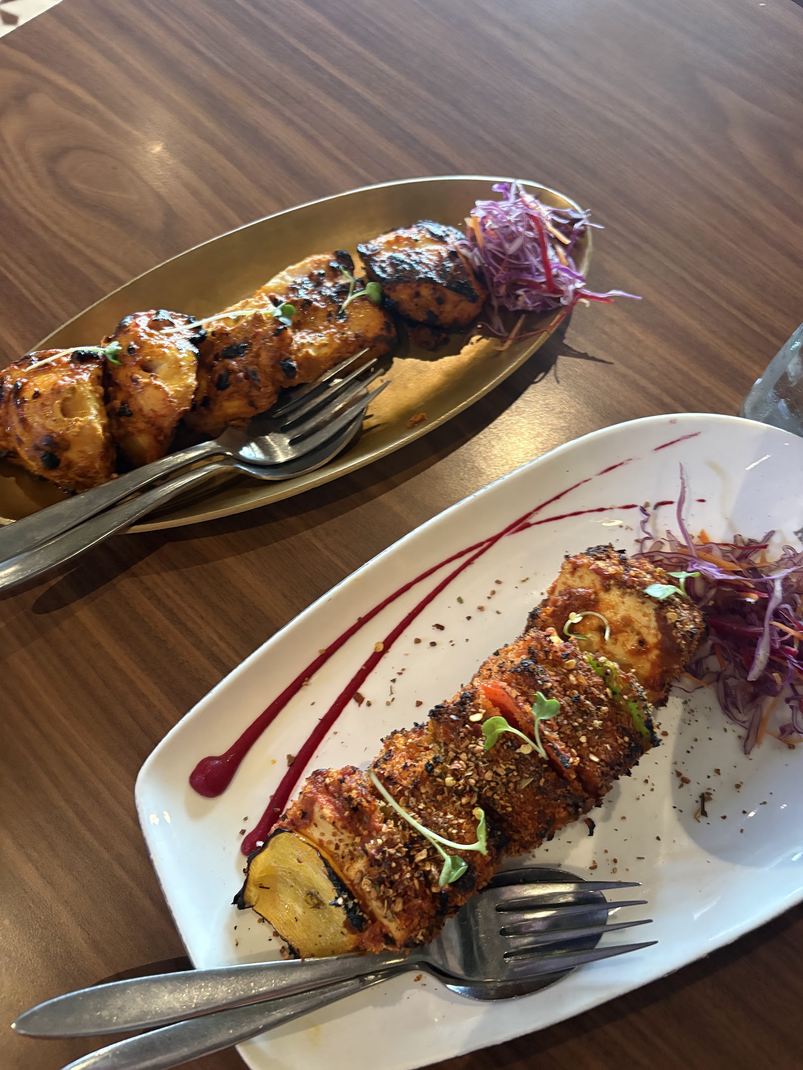 Two plates of grilled kebabs with onion, lime and mint on a wooden table