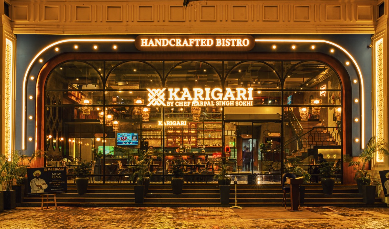 A Karigari restaurant at night, its arched glass front glowing, under a Handcrafted Bistro sign